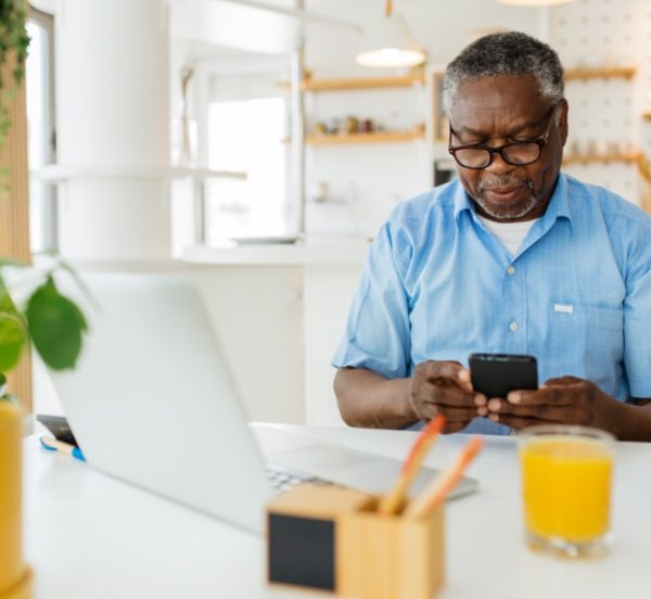 Man sitting at his home office and using his phone in front of his laptop